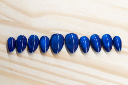 Deep blue cat eye effect press on nails featured on a wooden background