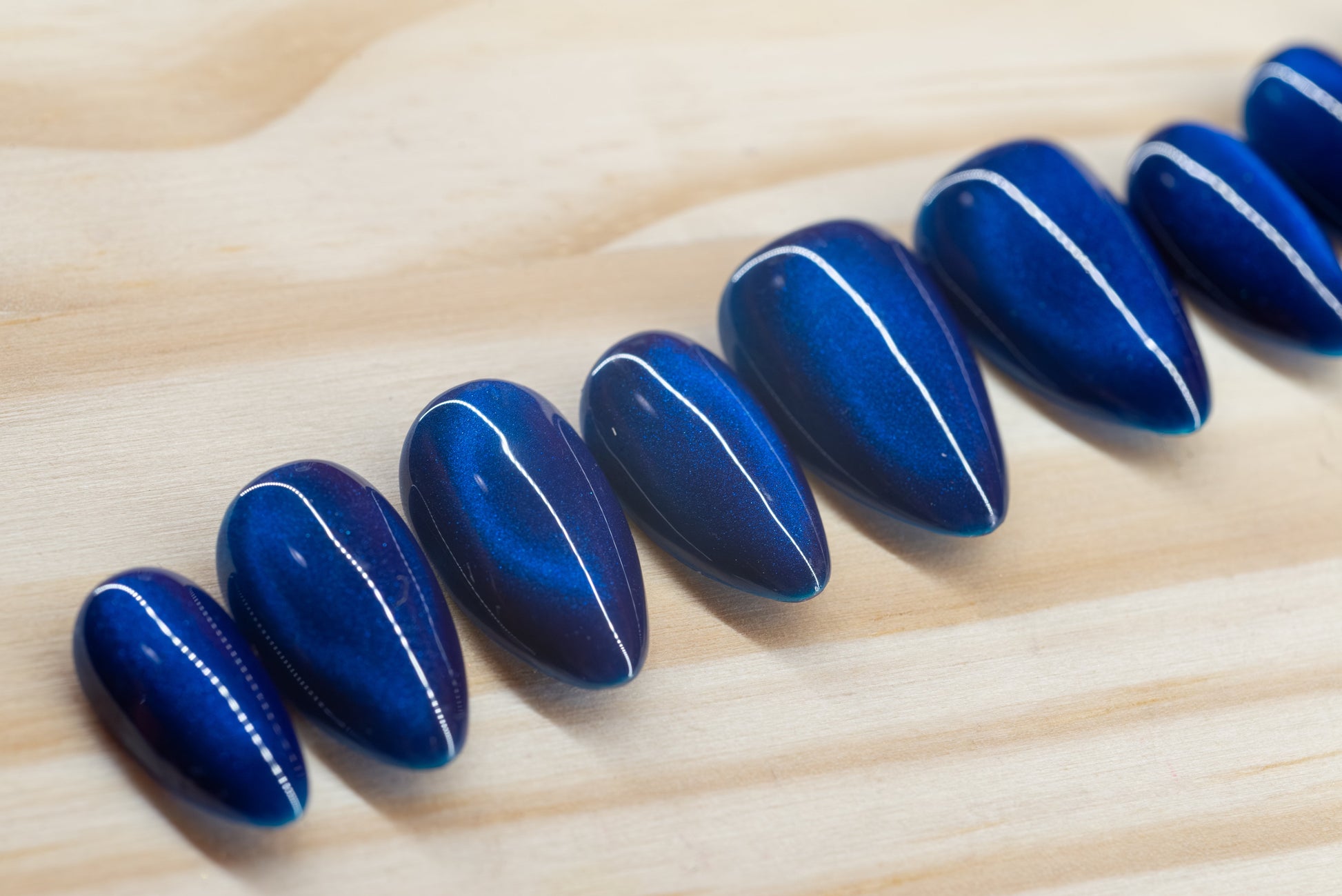 Deep blue cat eye effect press on nails featured on a wooden background