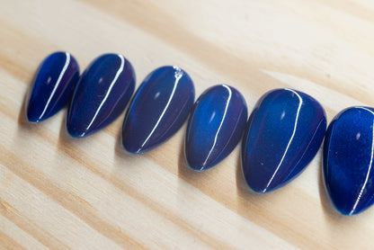 Deep blue cat eye effect press on nails featured on a wooden background