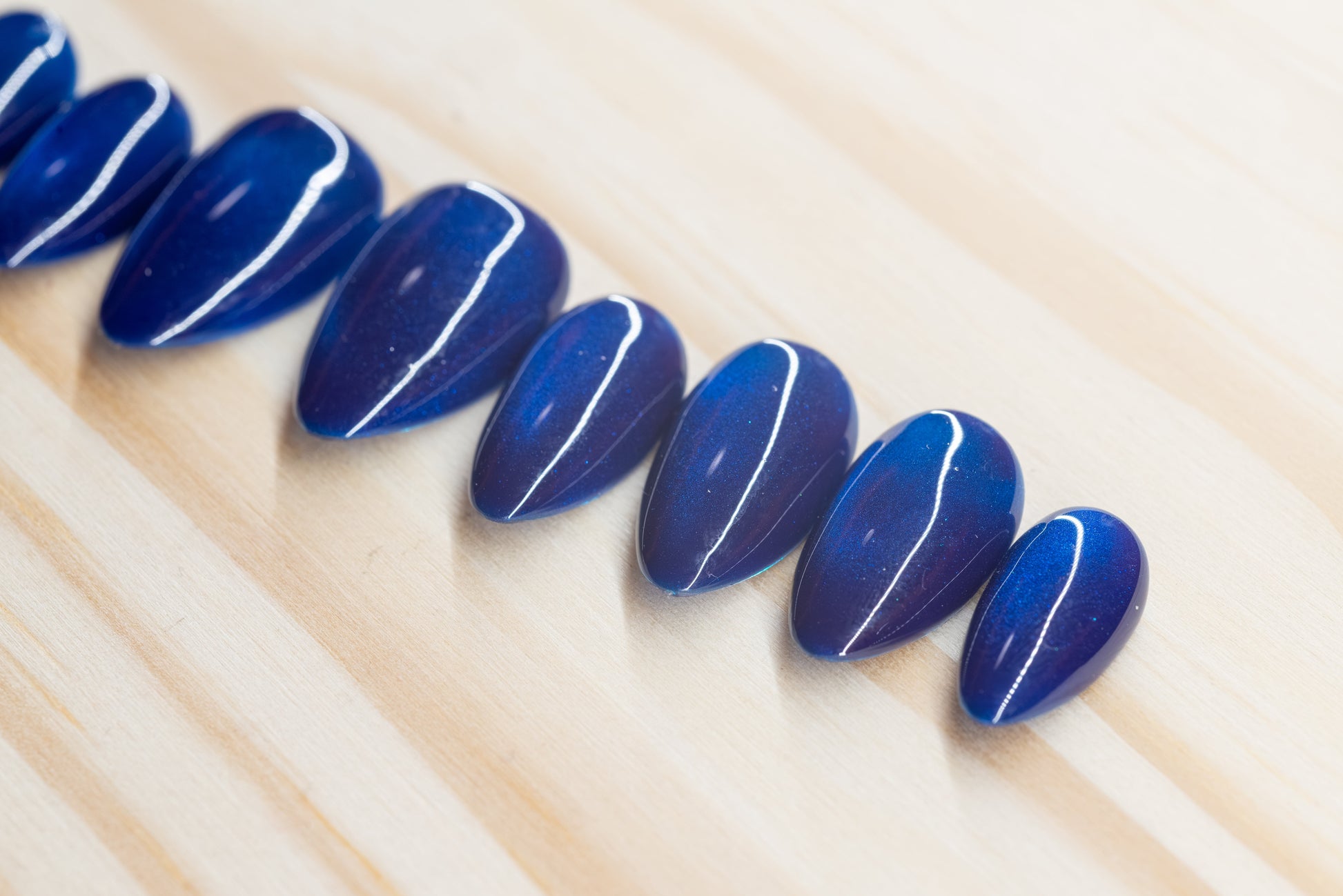 Deep blue cat eye effect press on nails featured on a wooden background
