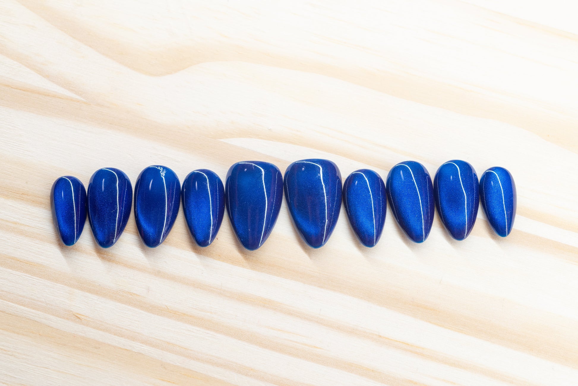 Deep blue cat eye effect press on nails featured on a wooden background