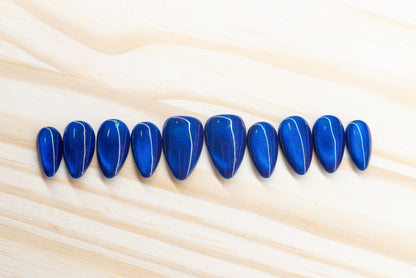 Deep blue cat eye effect press on nails featured on a wooden background