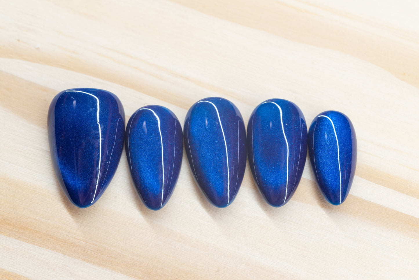 Deep blue cat eye effect press on nails featured on a wooden background