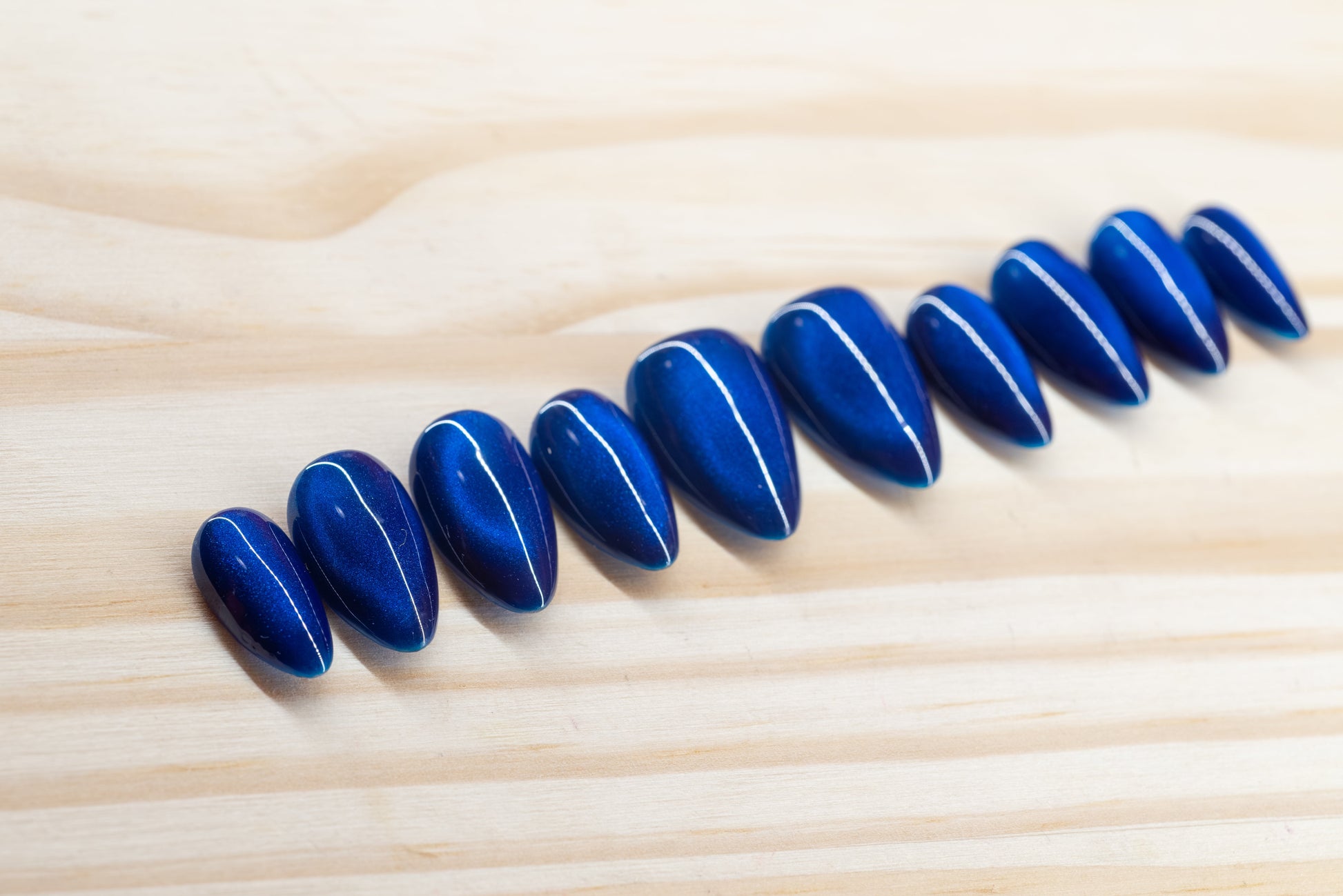 Deep blue cat eye effect press on nails featured on a wooden background