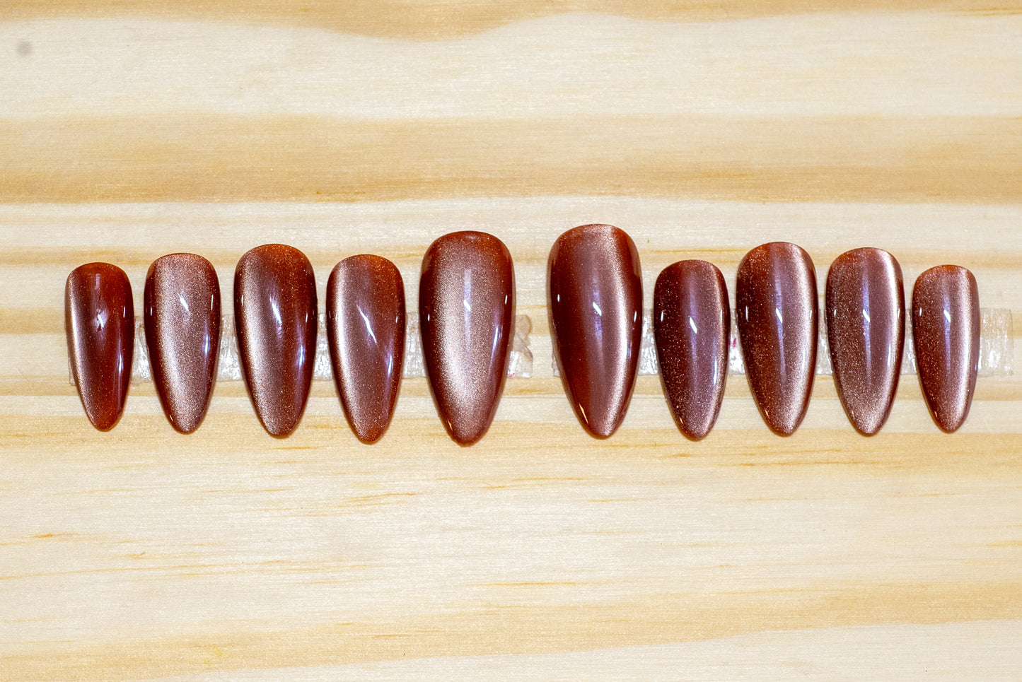 Dusty rose colored cat eye effect press on nails featured on a wooden background