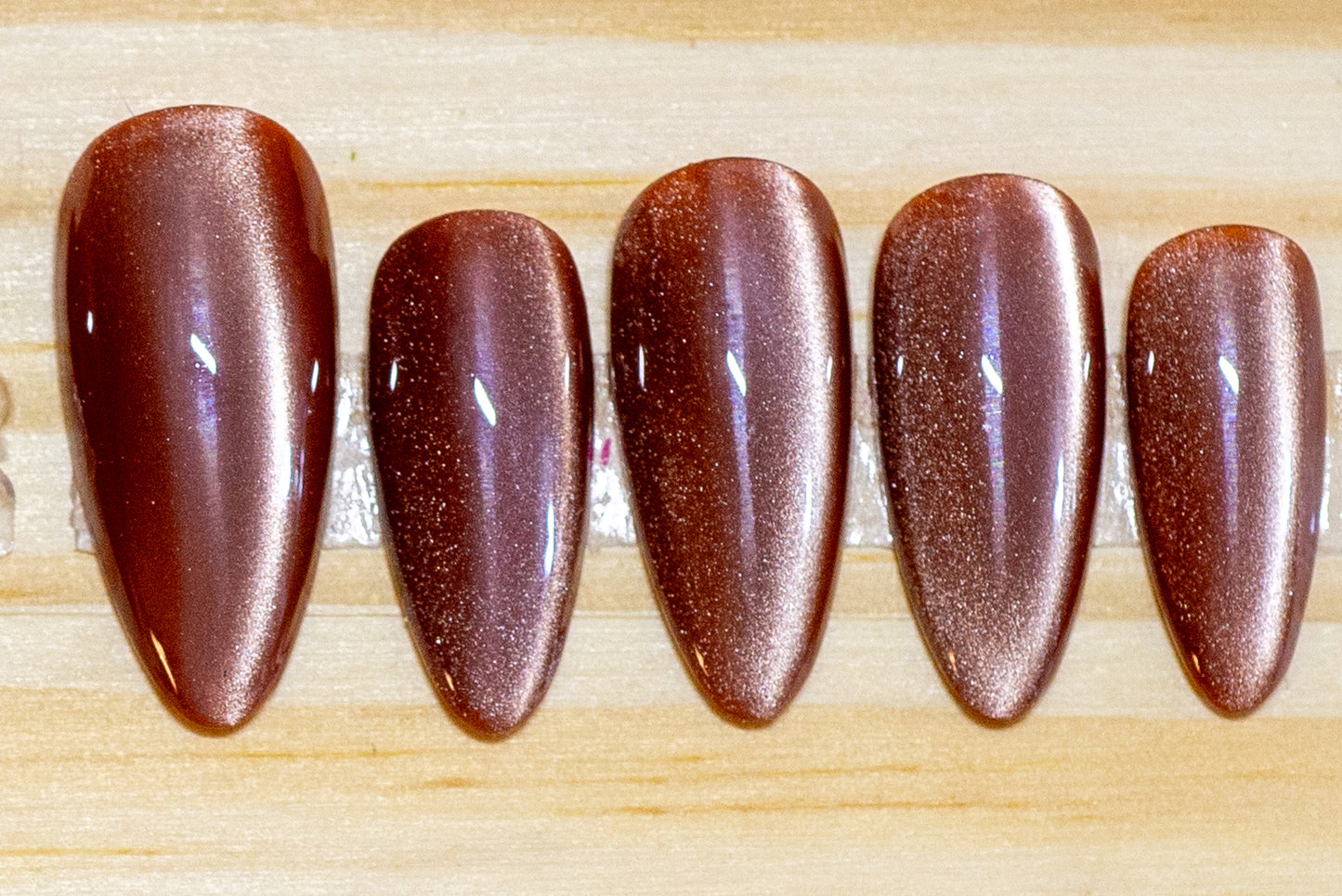 Dusty rose colored cat eye effect press on nails featured on a wooden background