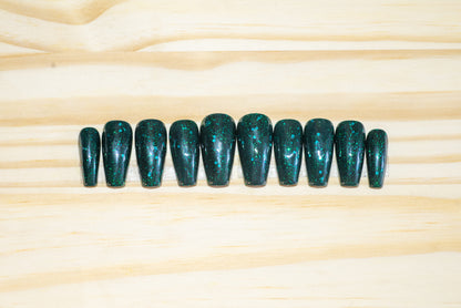 Glittery emerald green press on nails featured on a wooden background