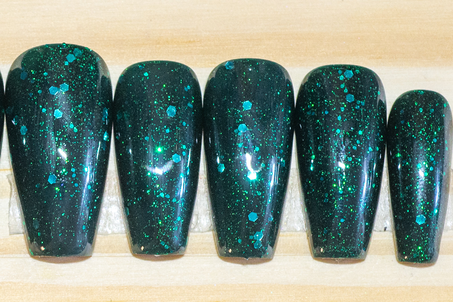 Glittery emerald green press on nails featured on a wooden background
