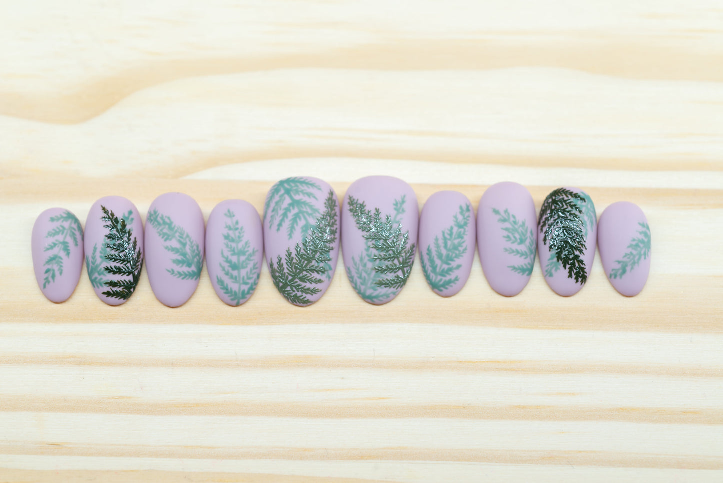 Mauve press on nails with fern motif featured on a wooden background