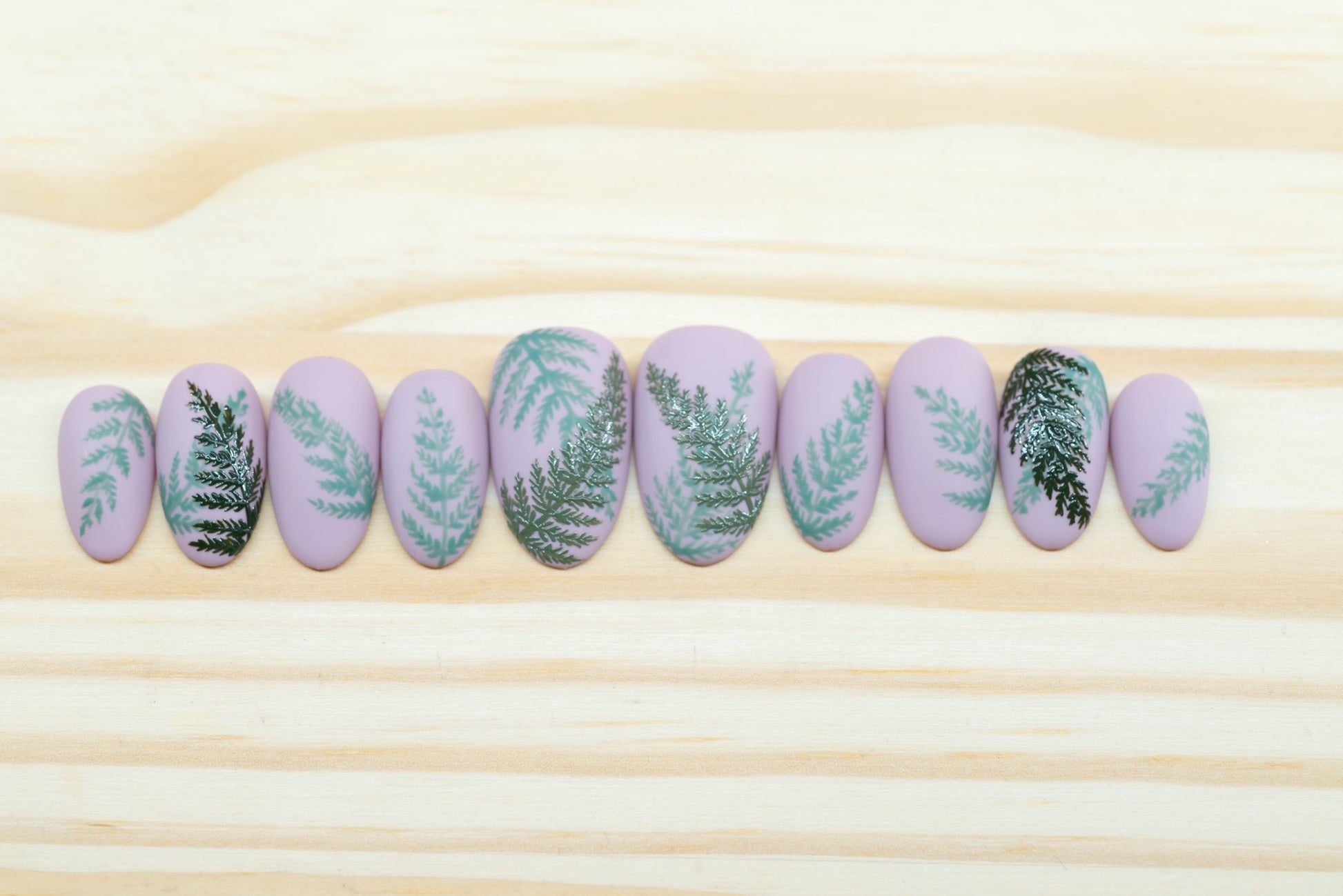 Mauve press on nails with fern motif featured on a wooden background