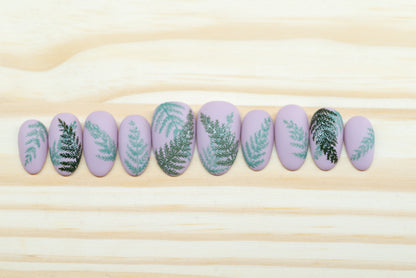 Mauve press on nails with fern motif featured on a wooden background