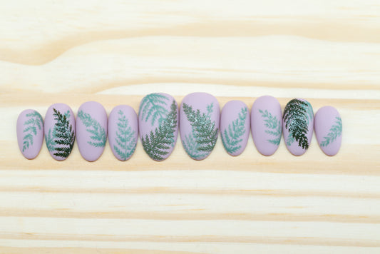 Mauve press on nails with fern motif featured on a wooden background
