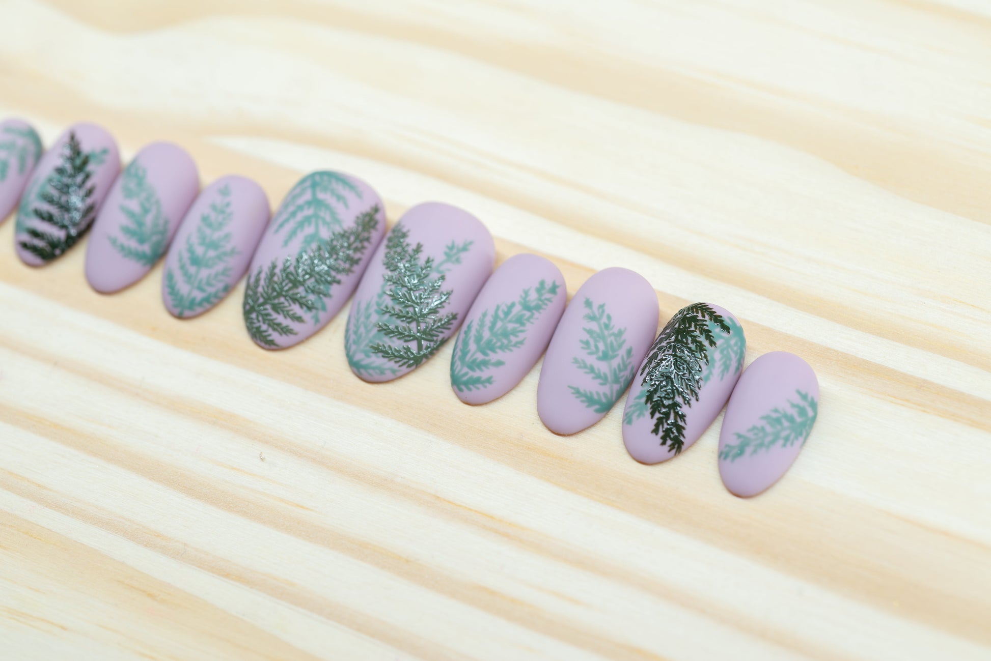 Mauve press on nails with fern motif featured on a wooden background
