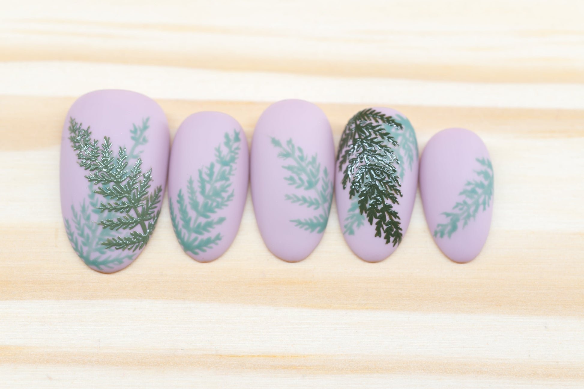 Mauve press on nails with fern motif featured on a wooden background