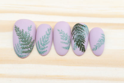 Mauve press on nails with fern motif featured on a wooden background