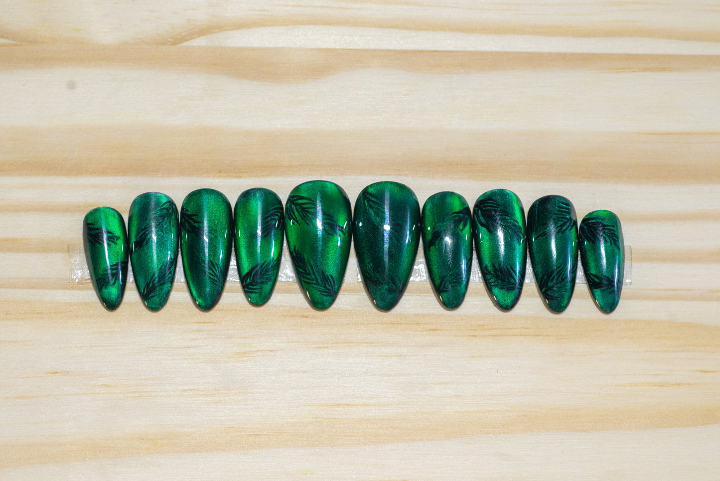Deep green cat eye press on nails with pine twig motif on a wooden background