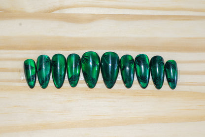 Deep green cat eye press on nails with pine twig motif on a wooden background
