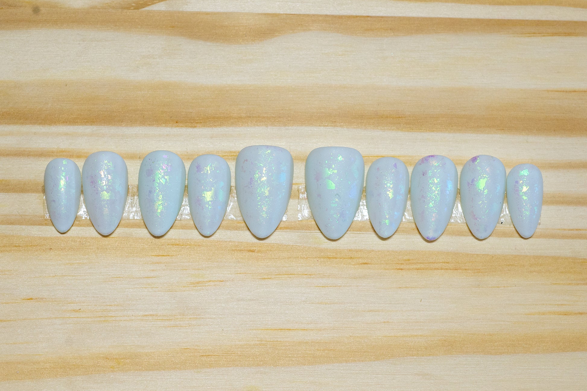 Pale mint green press on nails with green metallic flake and matte finish featured on a wooden background