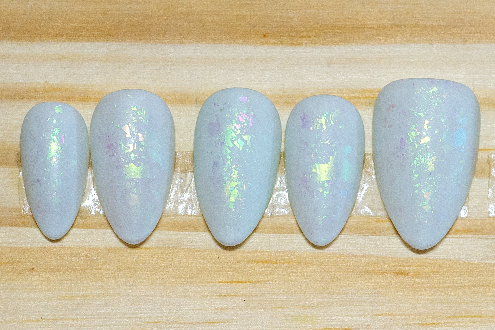 Pale mint green press on nails with green metallic flake and matte finish featured on a wooden background