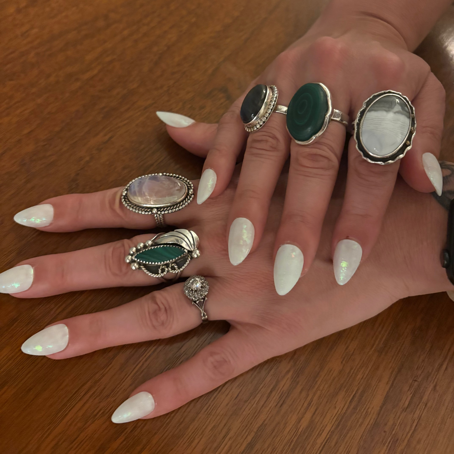 hands wearing natural stone rings and Icy white press on nails with shimmery green flakes