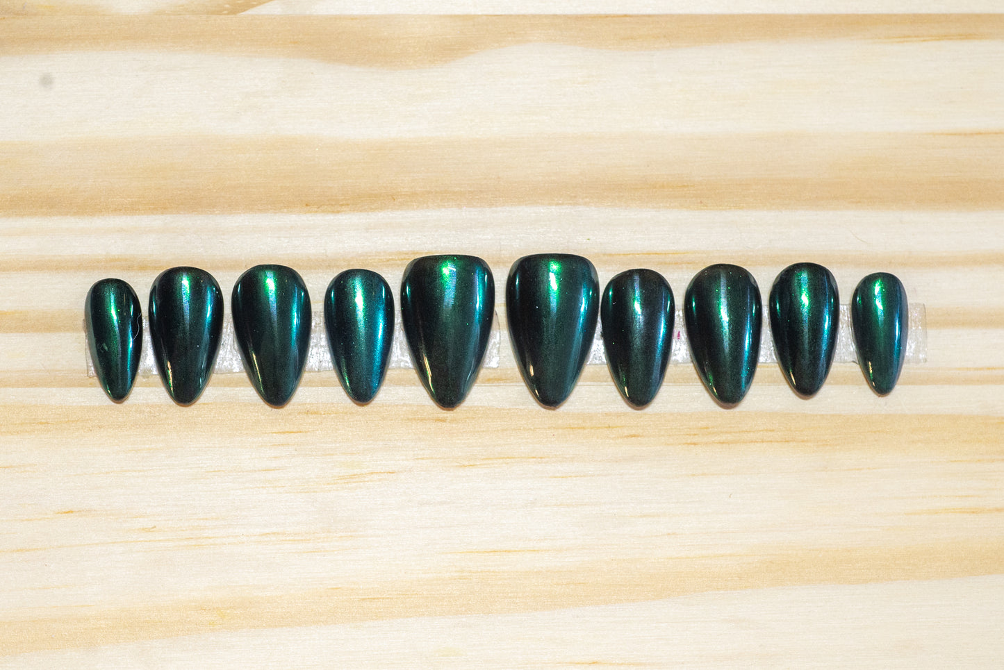 Metallic emerald green press on nails featured on a wooden background