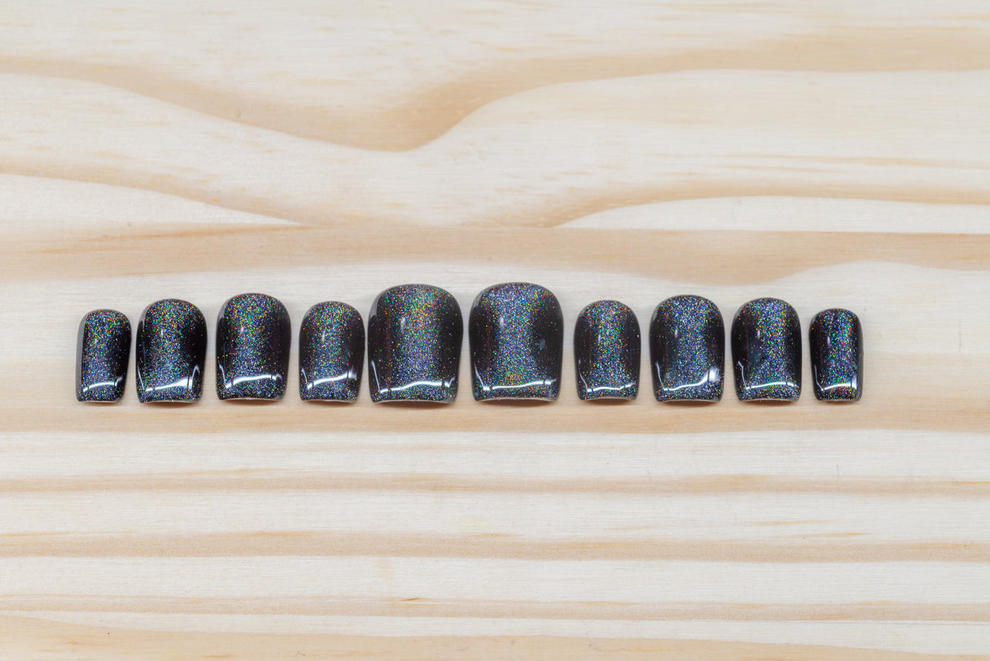 Black press on nails with hourglass-shaped holographic silver cat eye overlay featured on a wooden background