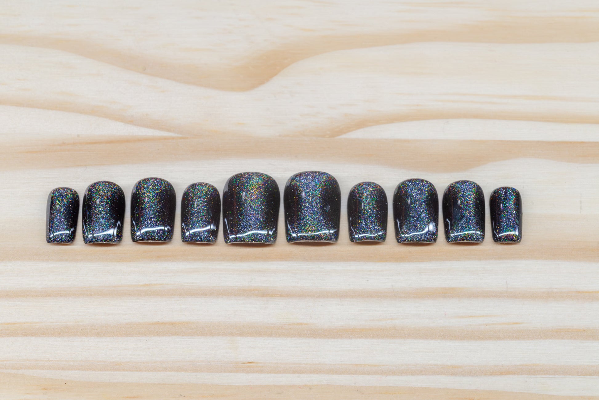 Black press on nails with hourglass-shaped holographic silver cat eye overlay featured on a wooden background