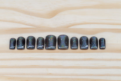 Black press on nails with hourglass-shaped holographic silver cat eye overlay featured on a wooden background