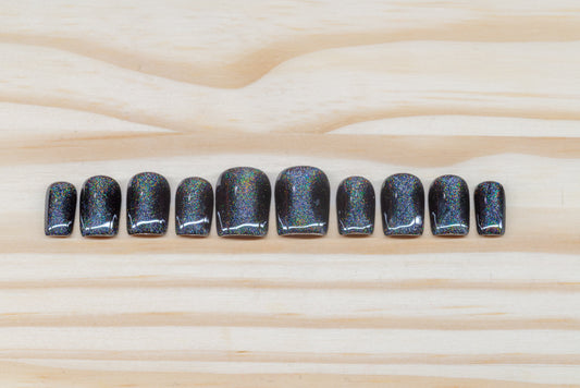 Black press on nails with hourglass-shaped holographic silver cat eye overlay featured on a wooden background