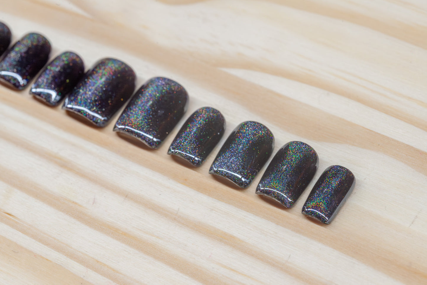 Black press on nails with hourglass-shaped holographic silver cat eye overlay featured on a wooden background