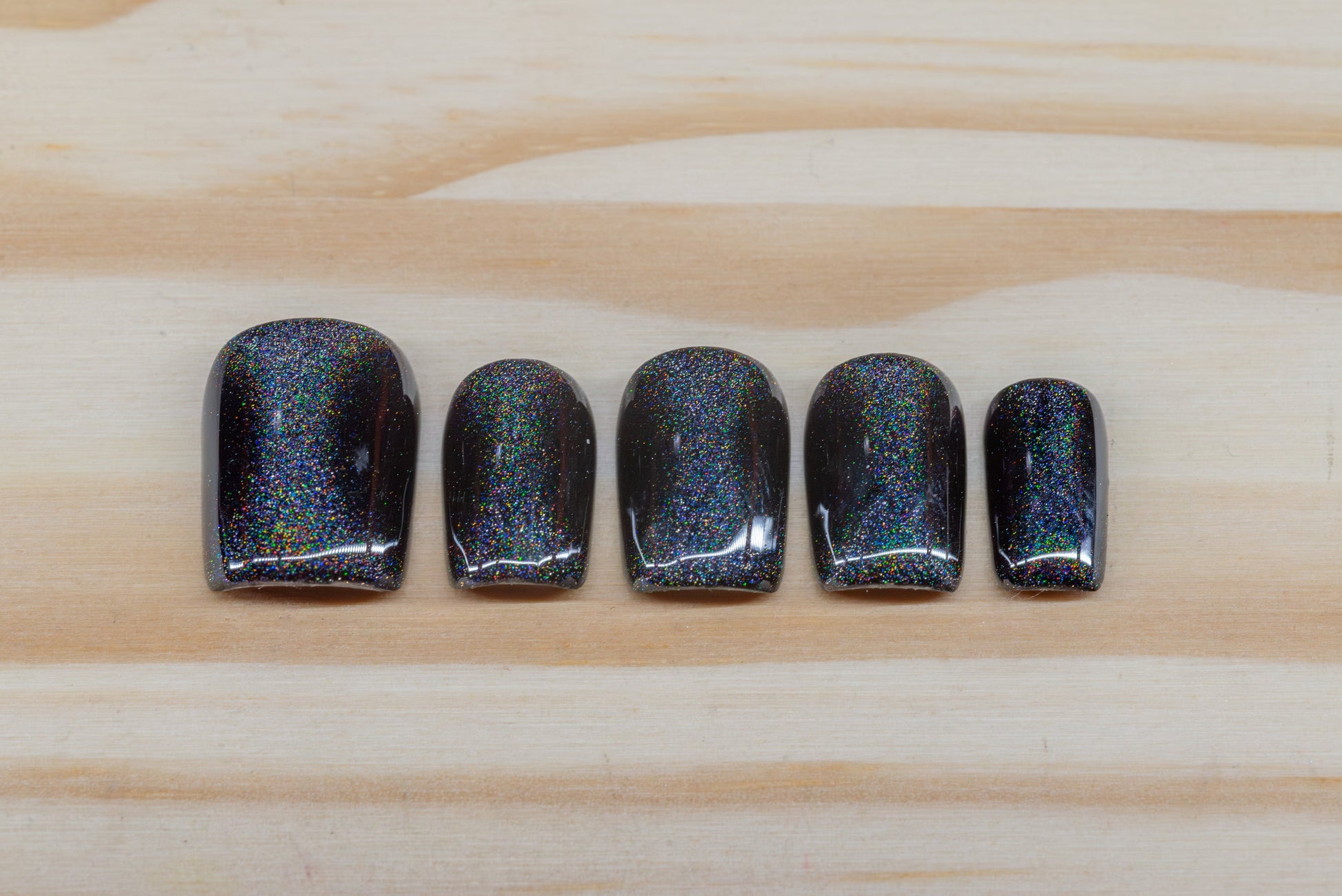 Black press on nails with hourglass-shaped holographic silver cat eye overlay featured on a wooden background