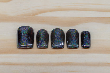 Black press on nails with hourglass-shaped holographic silver cat eye overlay featured on a wooden background