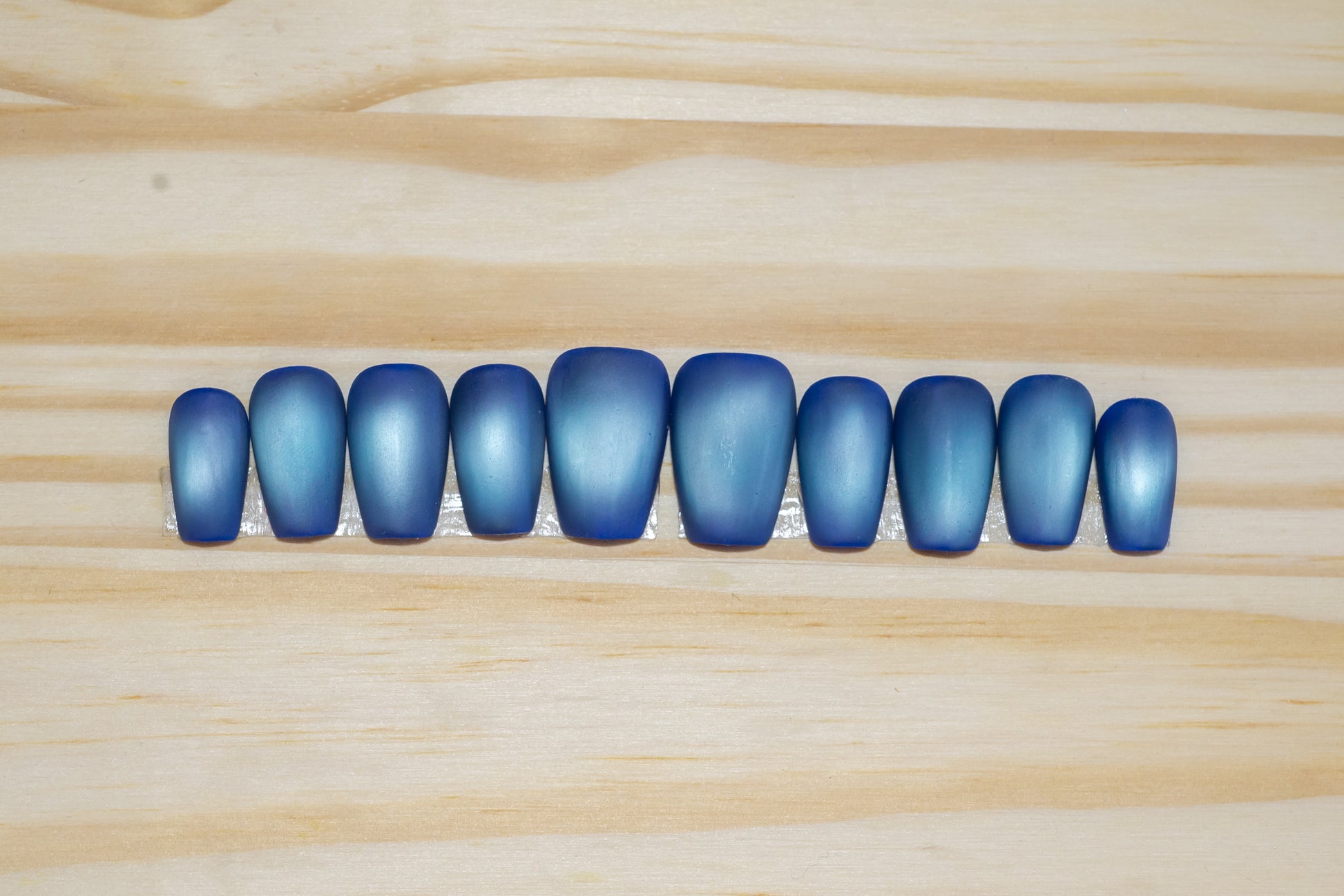 Deep blue with pale blue flash cat eye press on nails on a wooden background