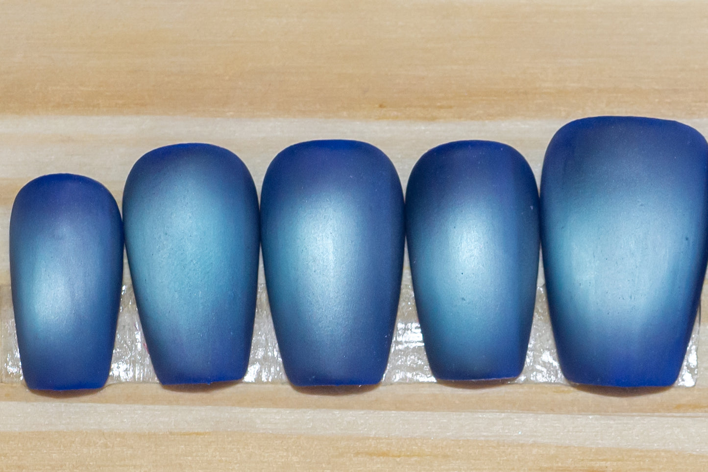 Deep blue with pale blue flash cat eye press on nails on a wooden background