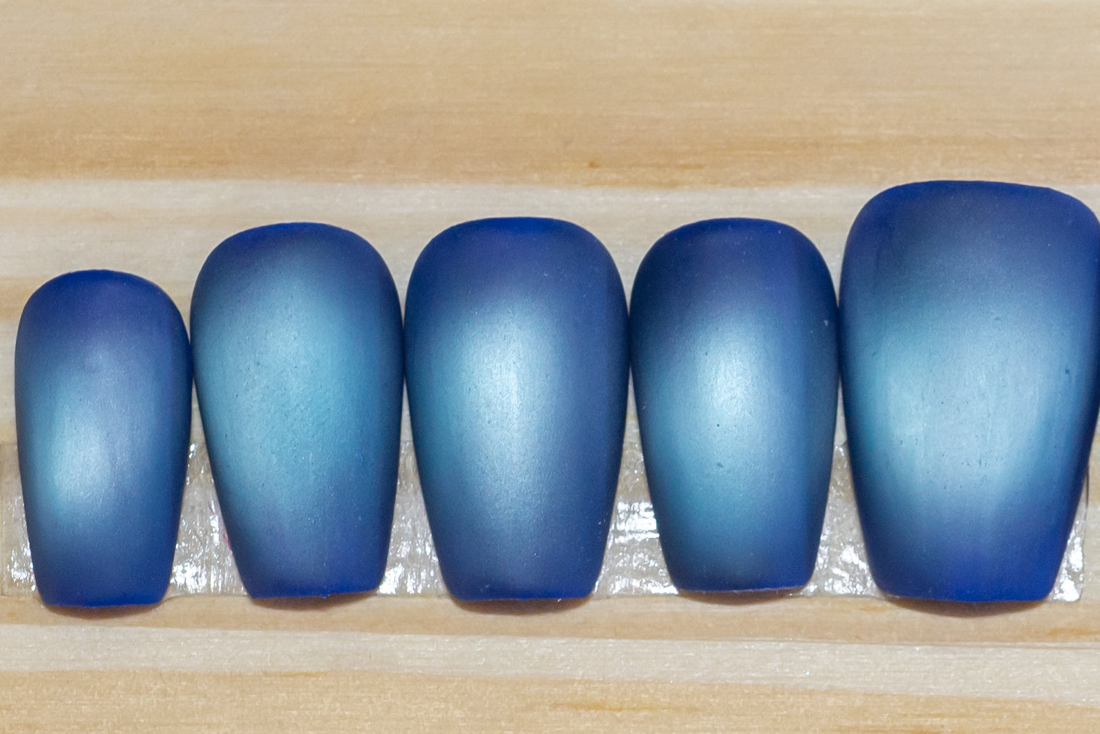 Deep blue with pale blue flash cat eye press on nails on a wooden background