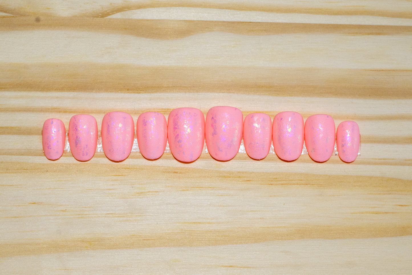 Peachy pink press on nails with pinky metallic flake and matte finish featured on a wooden background
