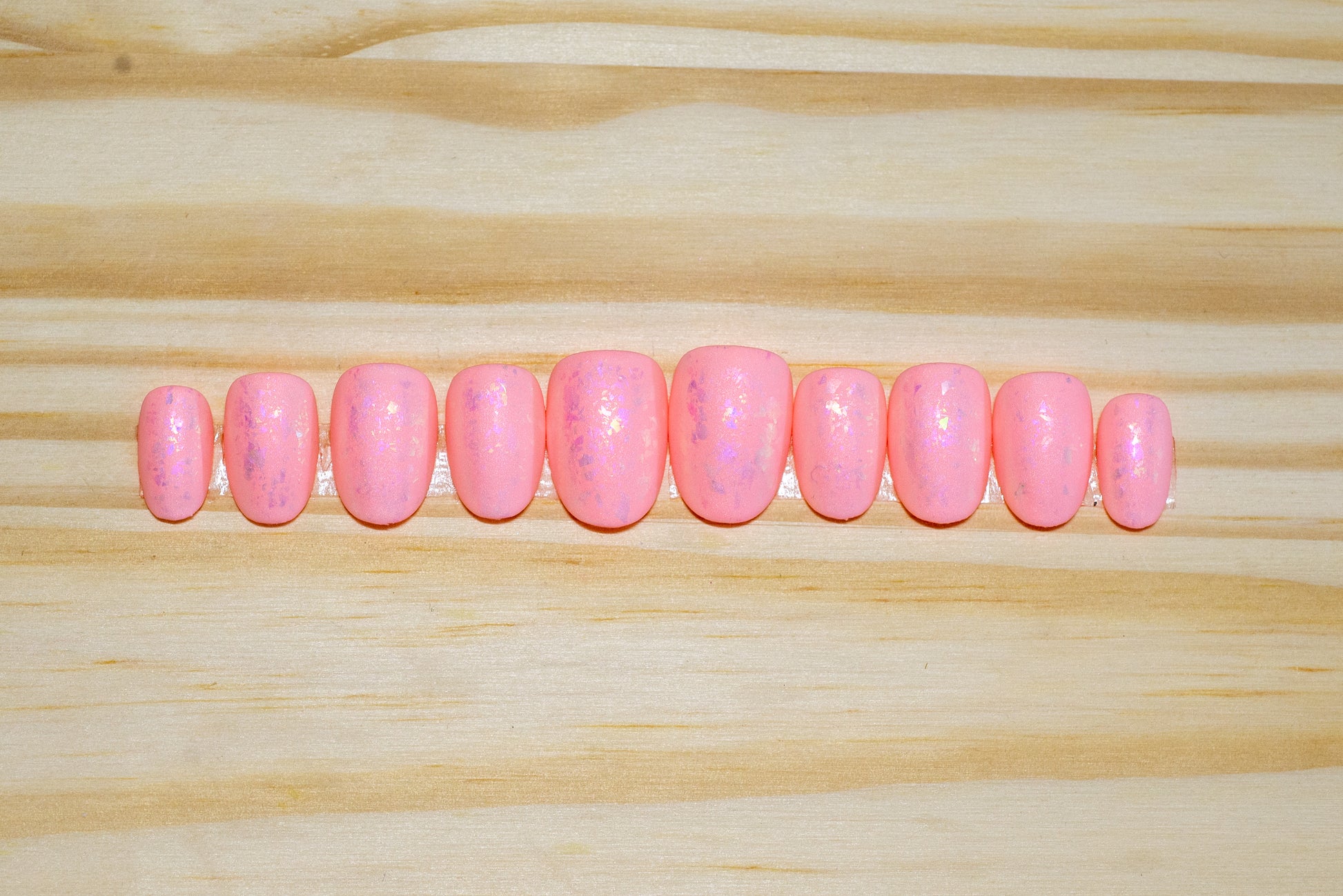 Peachy pink press on nails with pinky metallic flake and matte finish featured on a wooden background