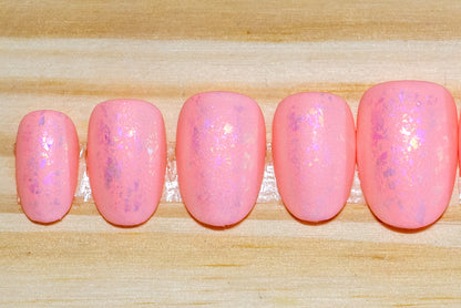 Peachy pink press on nails with pinky metallic flake and matte finish featured on a wooden background