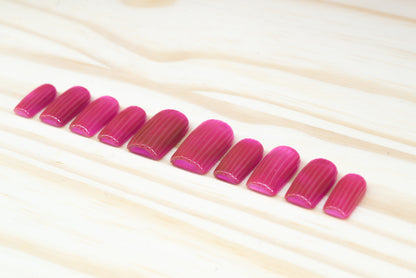 Pink cat eye press on nails that mimic fluted glass featured on a wooden background