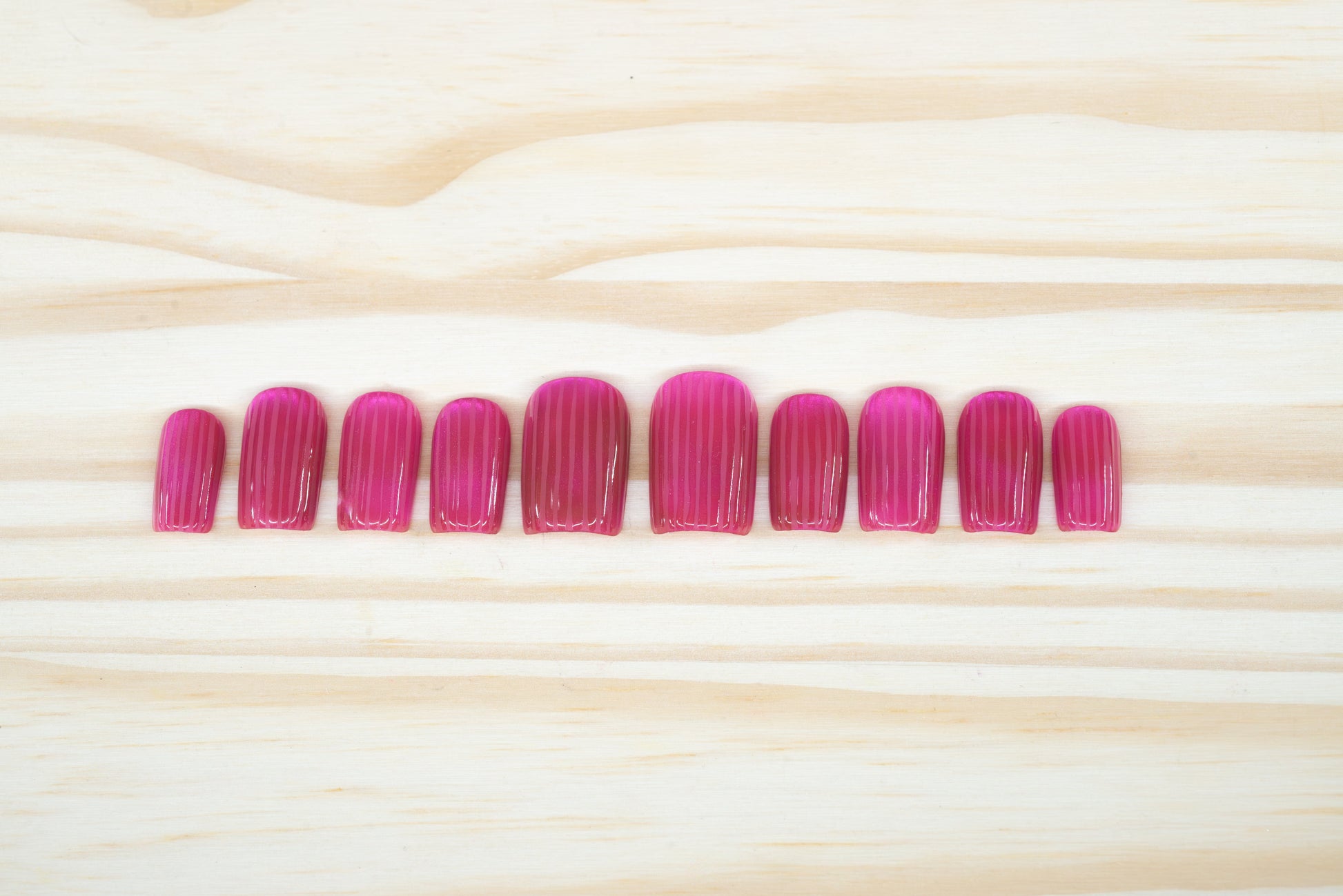 Pink cat eye press on nails that mimic fluted glass featured on a wooden background
