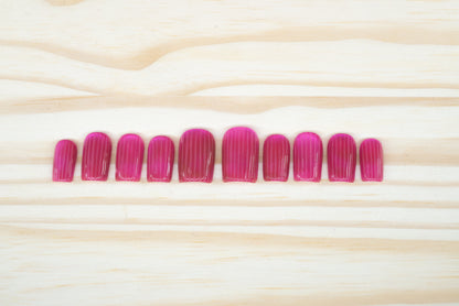 Pink cat eye press on nails that mimic fluted glass featured on a wooden background