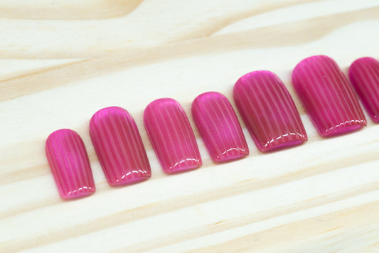 Pink cat eye press on nails that mimic fluted glass featured on a wooden background