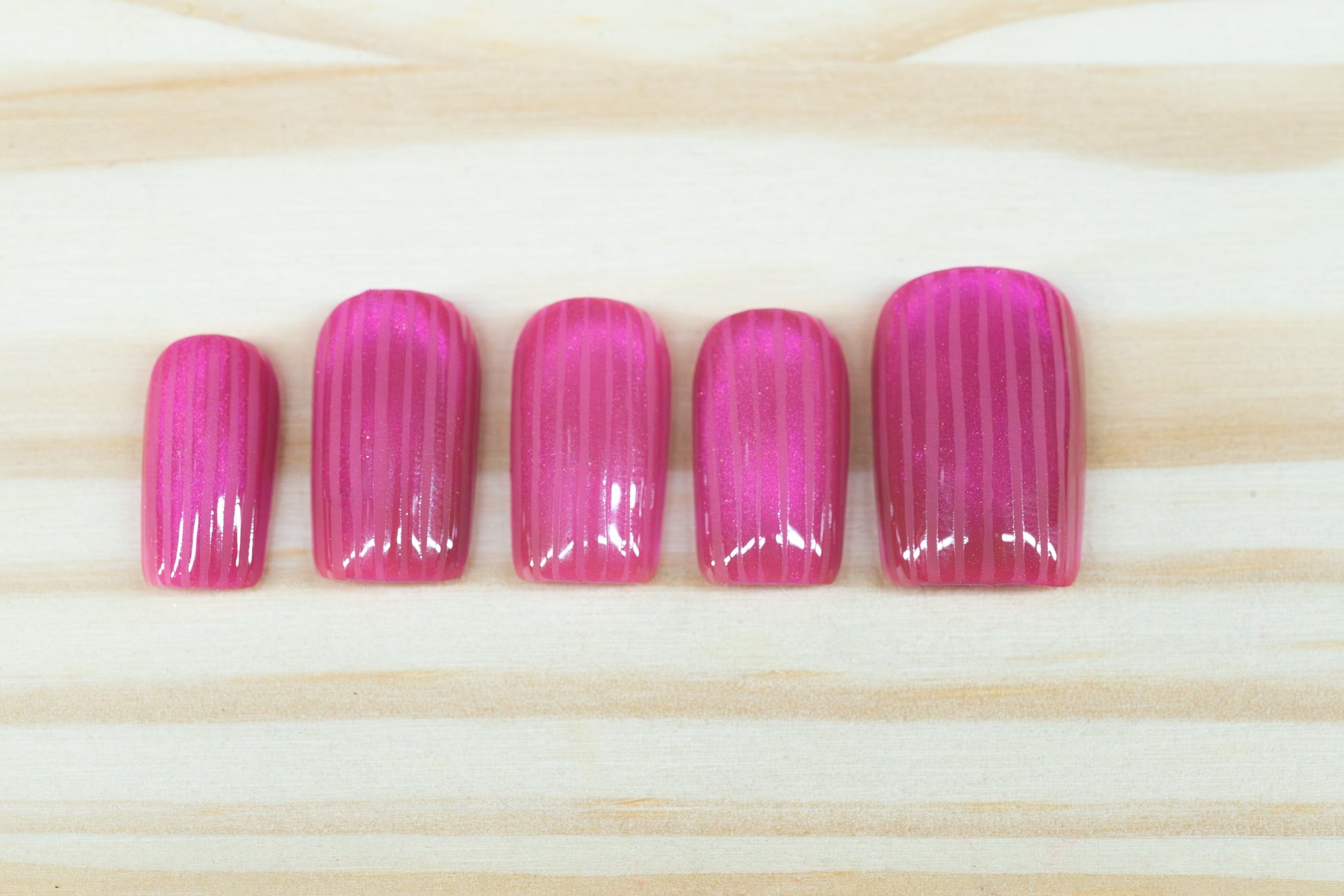 Pink cat eye press on nails that mimic fluted glass featured on a wooden background