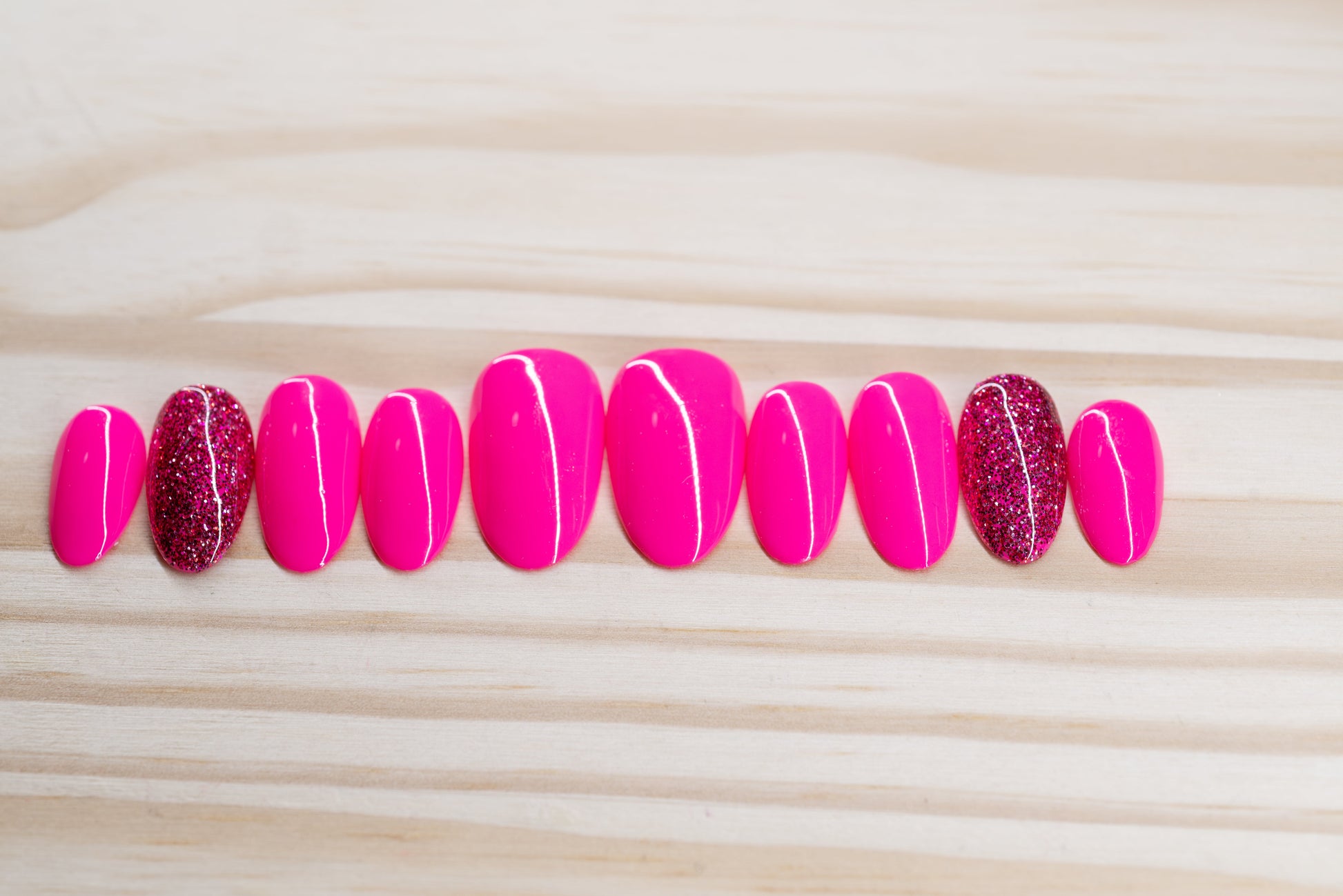 neon pink press on nails with one glitter nail each hand featured on a wooden background
