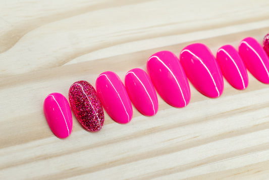neon pink press on nails with one glitter nail each hand featured on a wooden background
