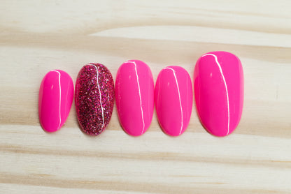 neon pink press on nails with one glitter nail each hand featured on a wooden background