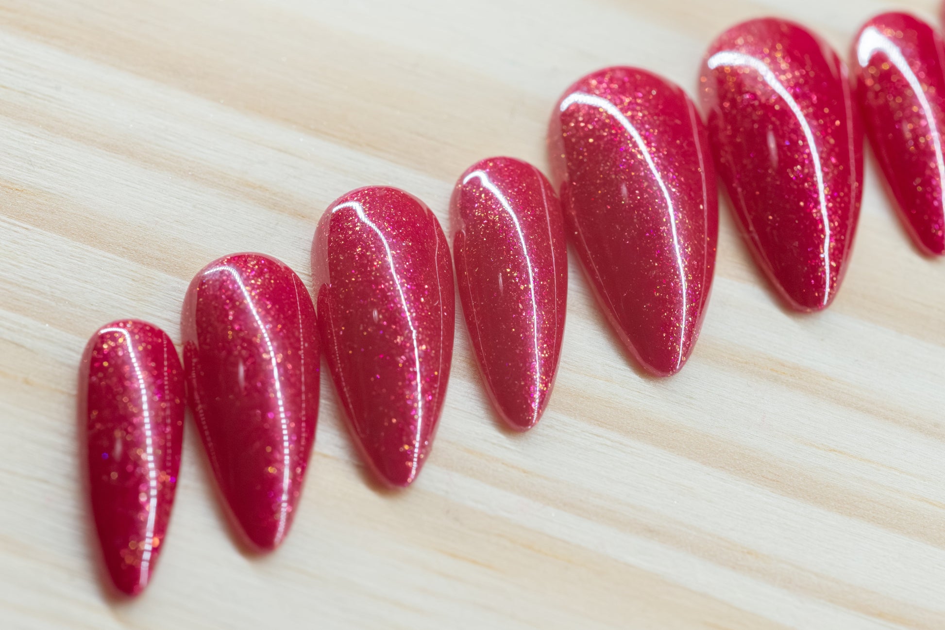 Sparkly berry pink press on nails featured on a wooden background