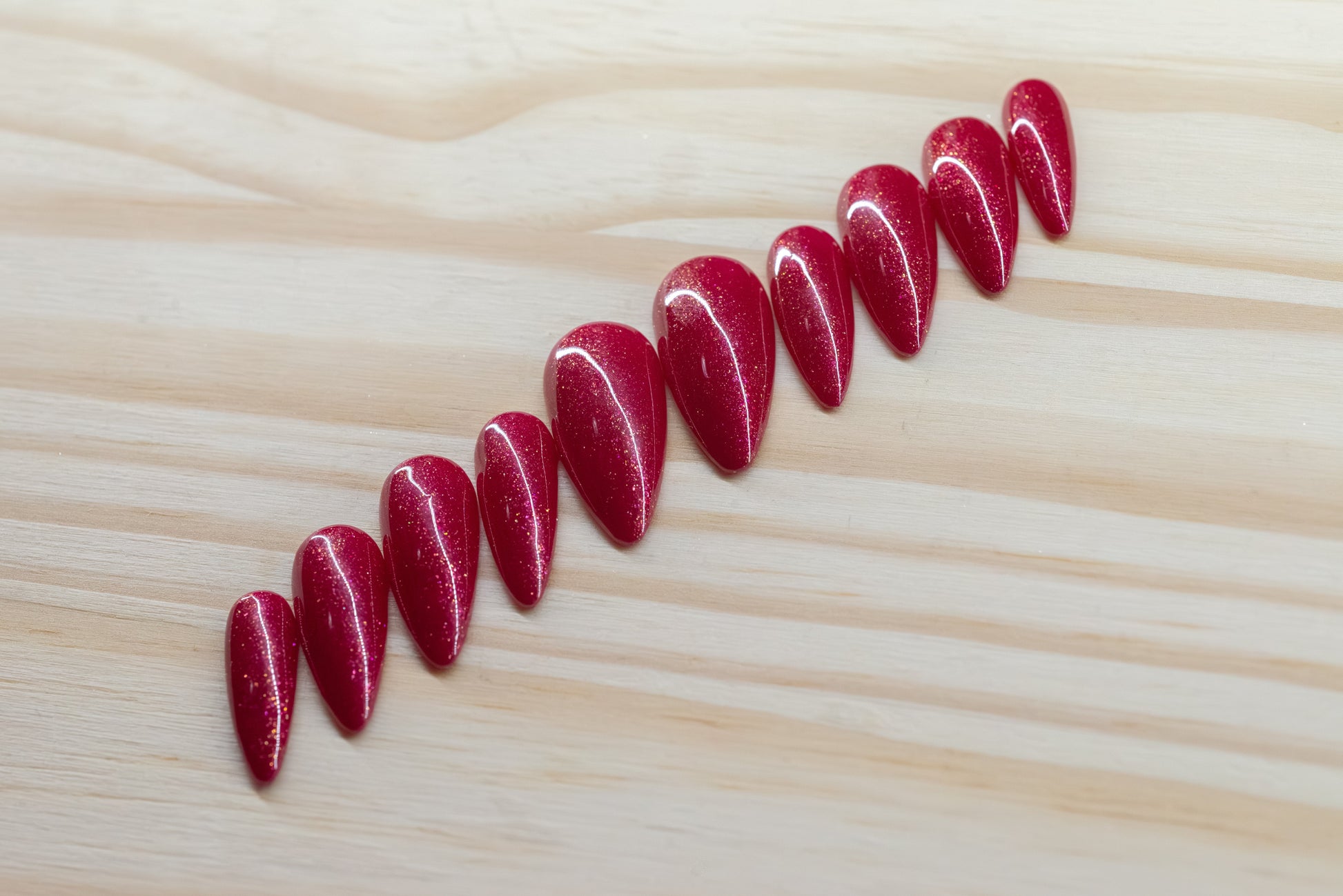 Sparkly berry pink press on nails featured on a wooden background