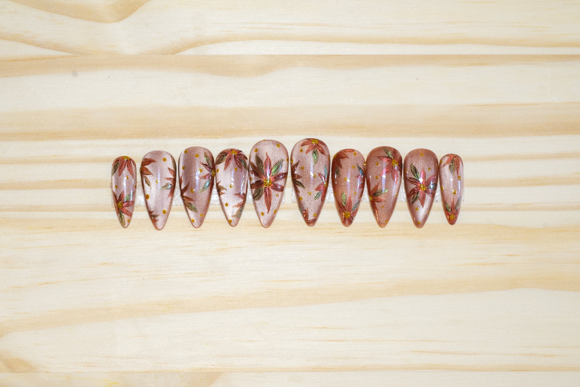 Hand-painted press on nails with chromed poinsettias on a neutral cateye base, featured on a wooden background