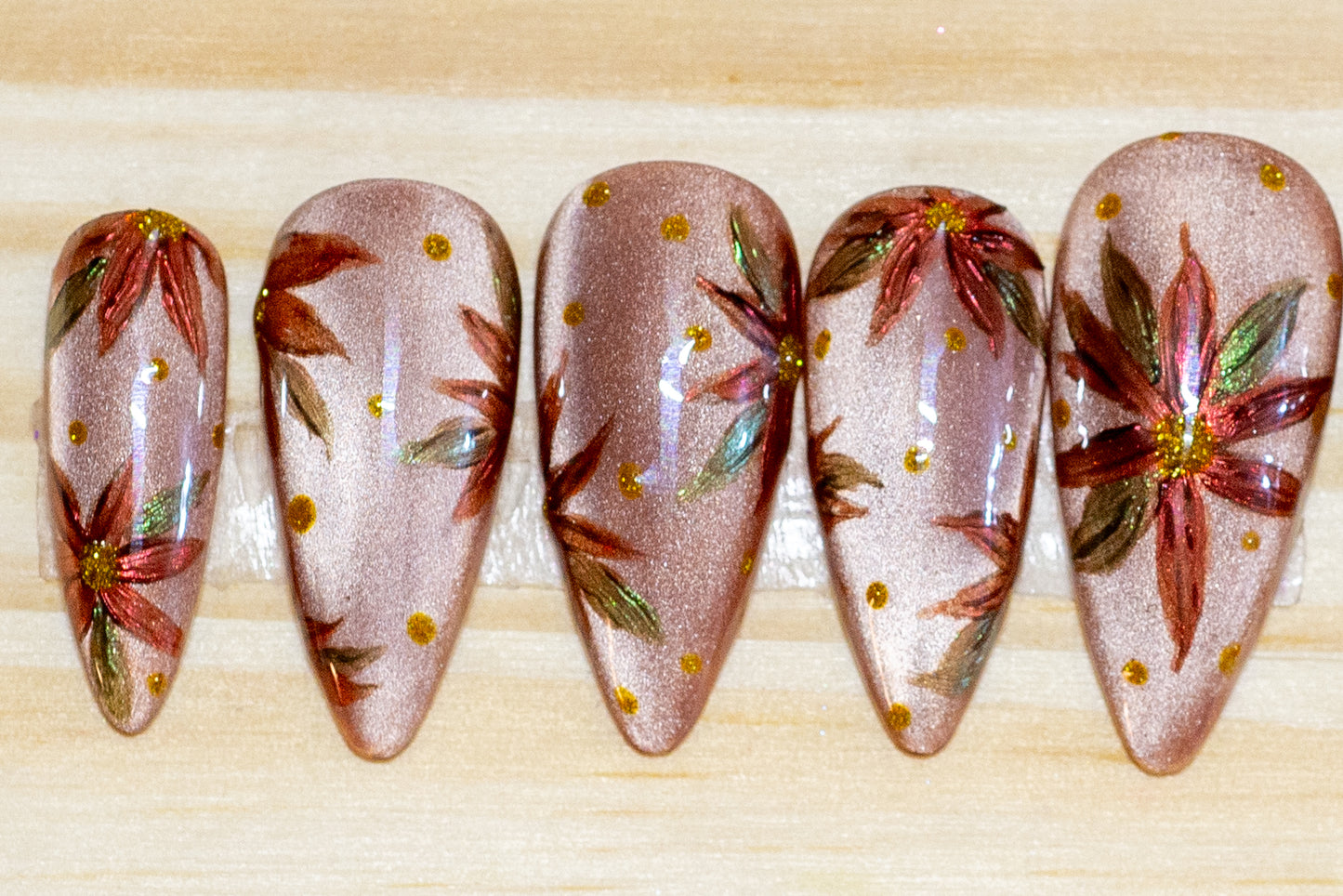 Hand-painted press on nails with chromed poinsettias on a neutral cateye base, featured on a wooden background